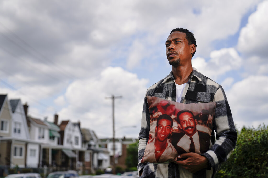 Brett Roman Williams poses for a photograph while holding a pillow with a photo of his father, Donald Williams, lower right, and brother Derrick Williams who both were killed by gunfire 20 years apart, in Philadelphia. (AP Photo/Matt Rourke)