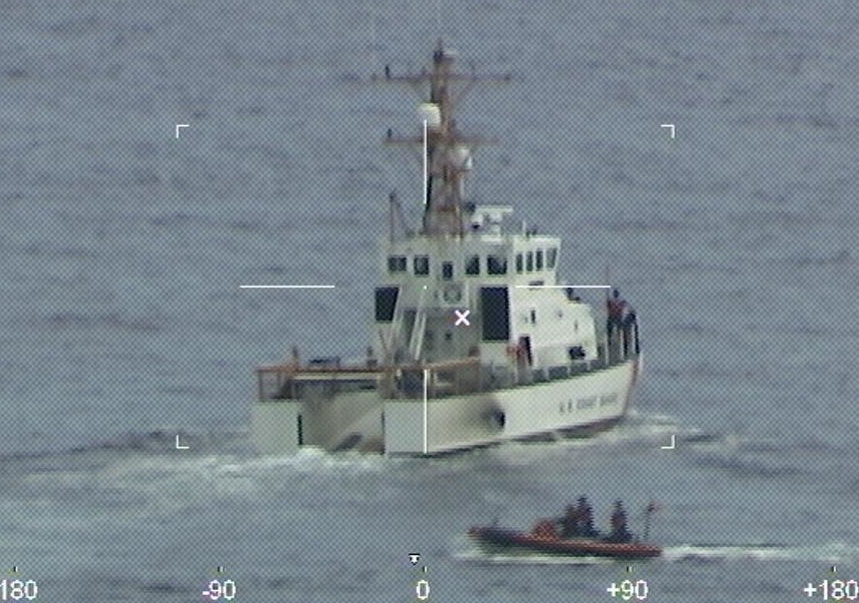 A coast guard ship in the ocean followed by a speed boat