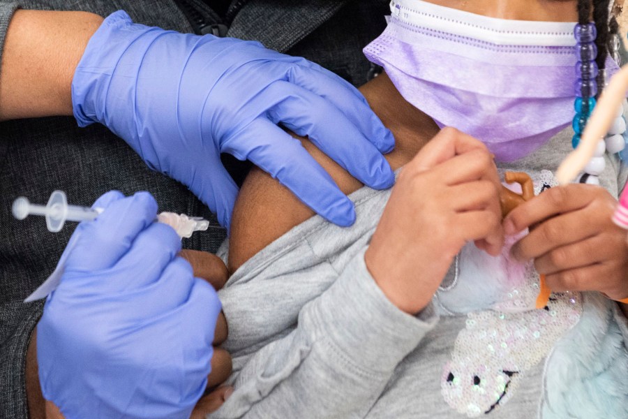 Gloved hands steady a young girl's shoulder as she receives a shot.