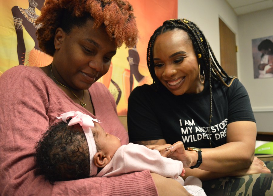 A woman in a pink shirt holds a baby as another woman looks on