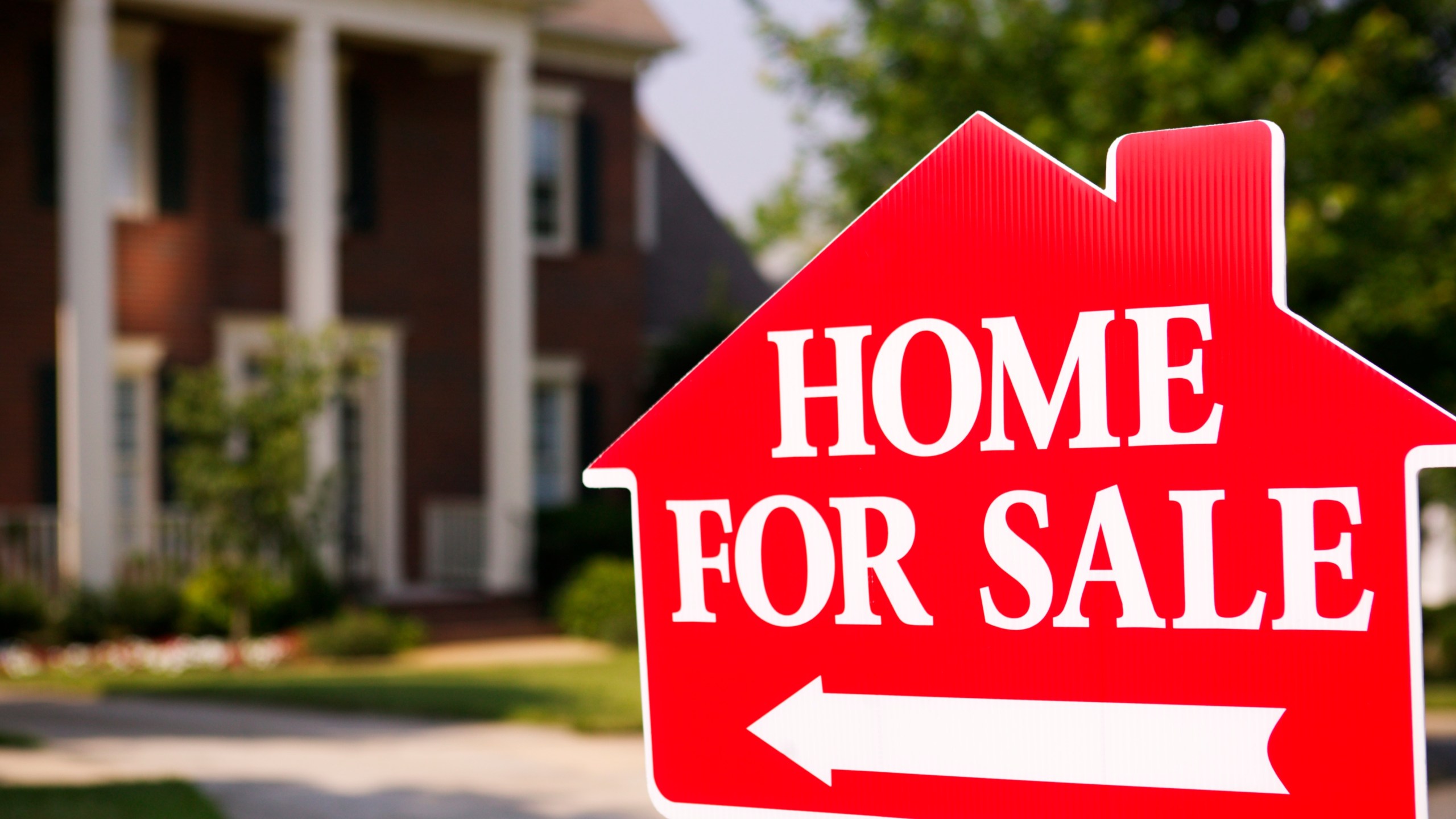 Close-up of a sign pointing to a home for sale in suburbia