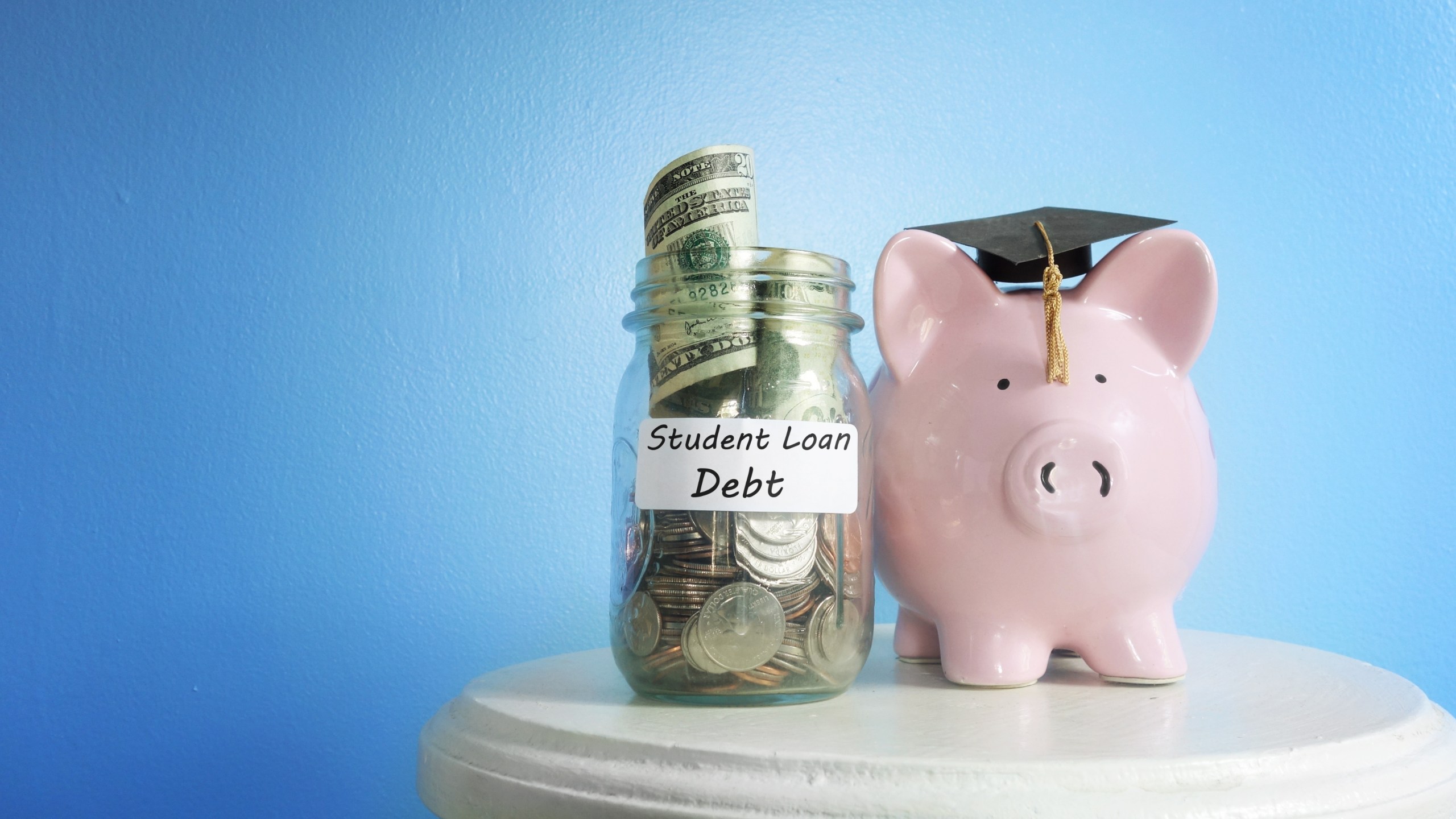 Piggy bank with graduation cap beside a student loan coin jar