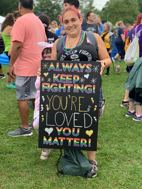 A woman holds a sign that says: Always keep fighting. You're loved, you matter.