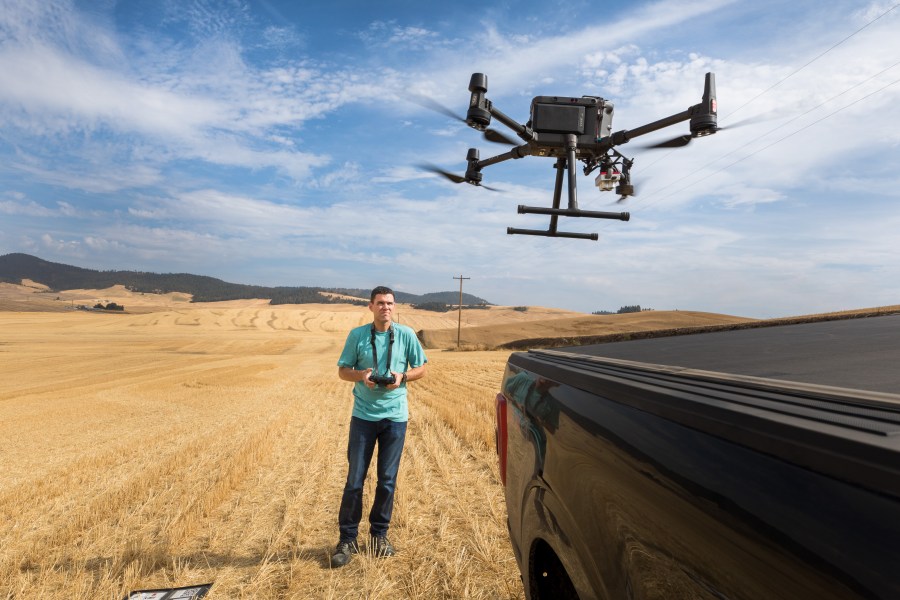 A man flies a drone over an empty farm field