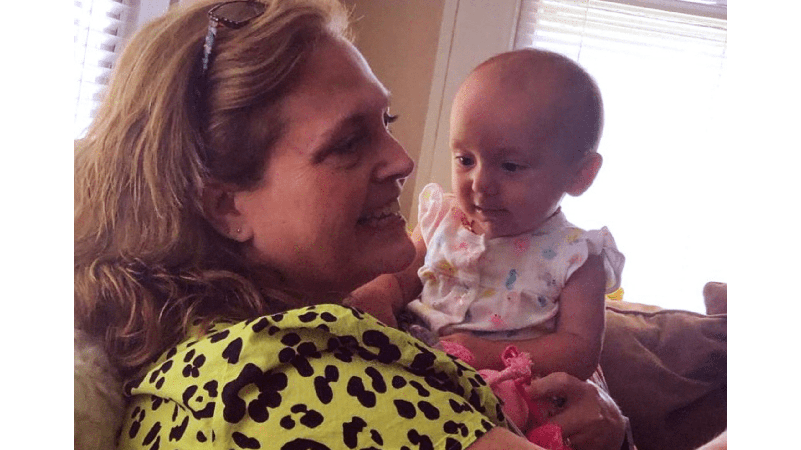 A woman with blond hair smiles as she holds a baby