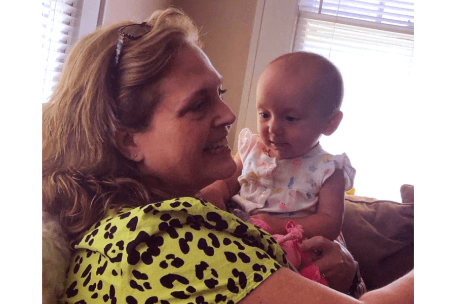 A woman with blond hair smiles as she holds a baby