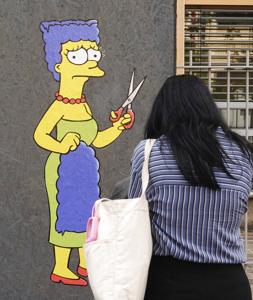 A woman takes pictures of a mural called "The Cut" by street artist aleXsandro Palombo depicting Marge Simpson, a character of the animated television series "The Simpsons" cutting her iconic hair, in front of the Consulate of Iran, in Milan, Italy, Wednesday, Oct. 5, 2022. Thousands of Iranians have taken to the streets over the last two weeks to protest the death of Mahsa Amini, a 22-year-old woman who had been detained by Iran's morality police in the capital of Tehran for allegedly not adhering to Iran's strict Islamic dress code. (AP Photo/Luca Bruno)