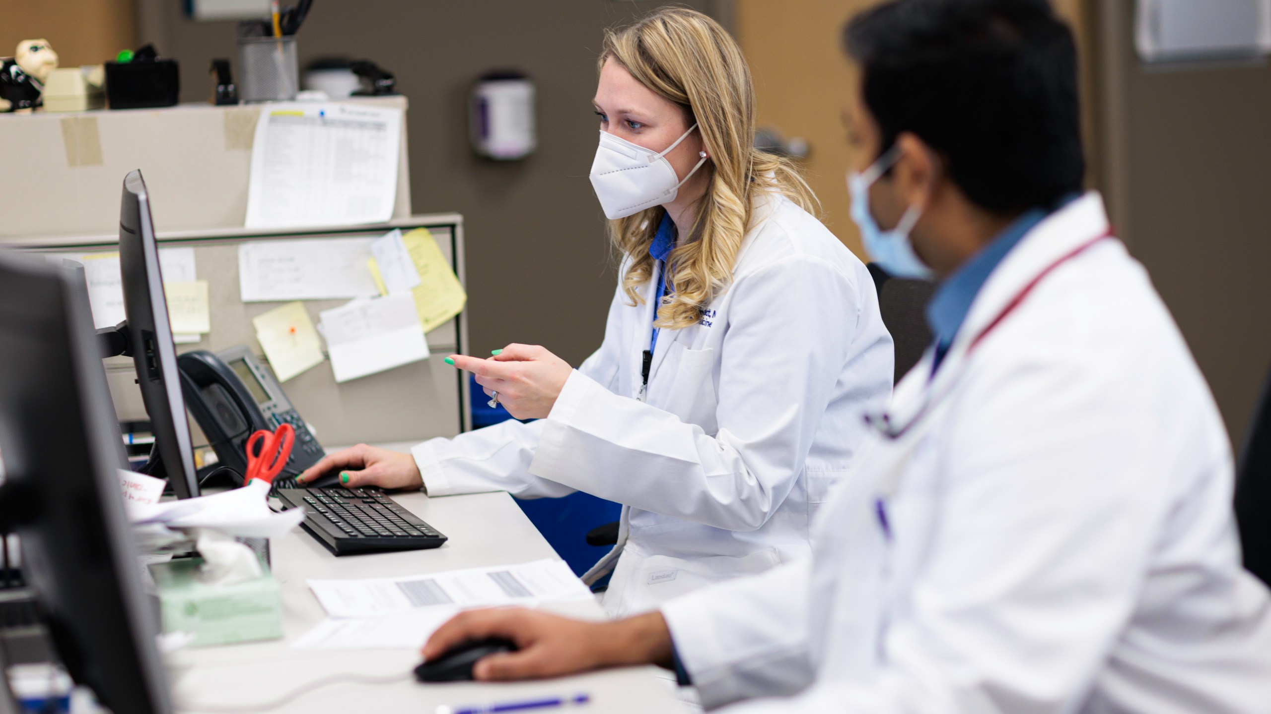 A woman and man doctor with masks on sit at a computer