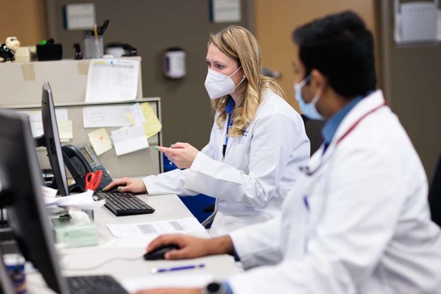 A woman and man doctor with masks on sit at a computer