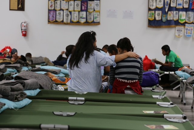 A woman puts her arm around another woman on a cot