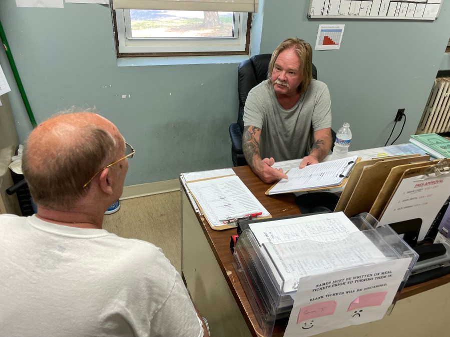 A man holds a clipboard while talking to another man