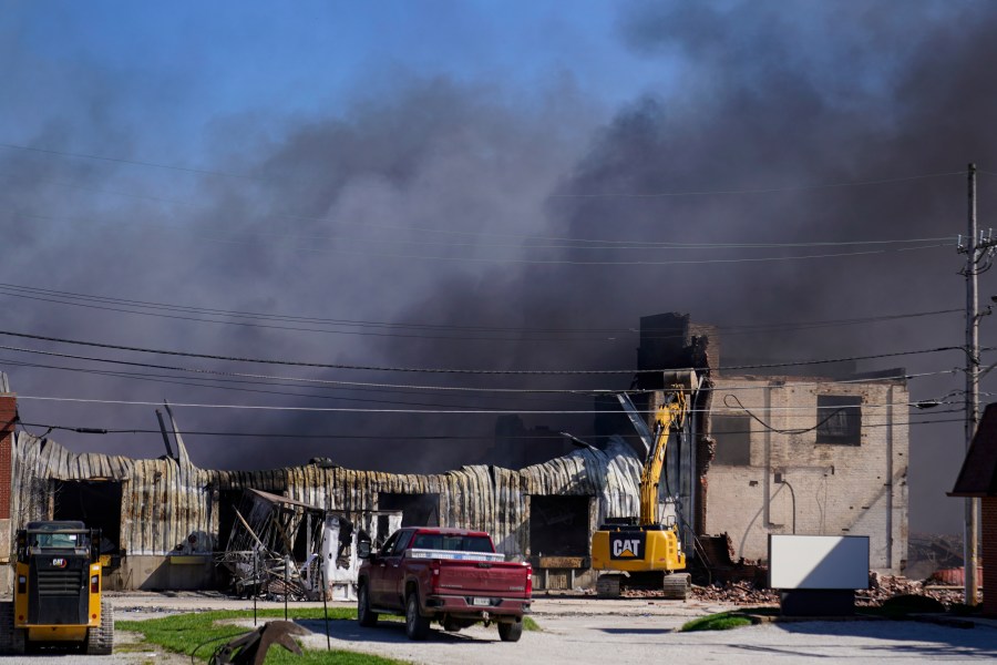 Workers knock down a section of site of an industrial fire the area as smoke billows from the site in Richmond, Ind., Wednesday, April 12, 2023. Authorities urged people to evacuate if they live near the fire. The former factory site was used to store plastics and other materials for recycling or resale. (AP Photo/Michael Conroy)