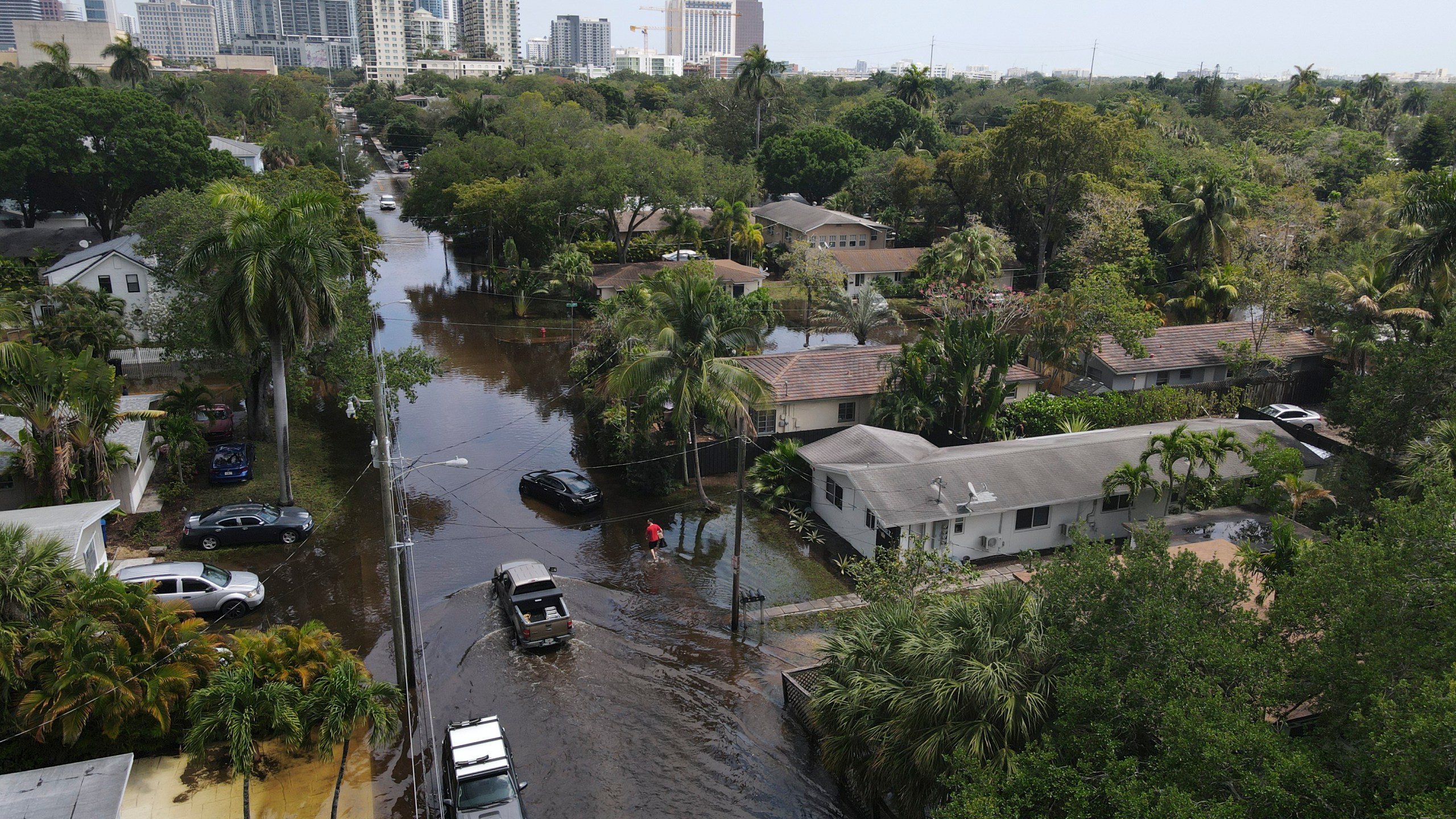 In this photo taken with a drone, trucks and a resident on foot make their way through receding floodwaters in the Sailboat Bend neighborhood of Fort Lauderdale, Fla., Thursday, April 13, 2023. Over 25 inches of rain fell in South Florida since Monday, causing widespread flooding. (AP Photo/Rebecca Blackwell)