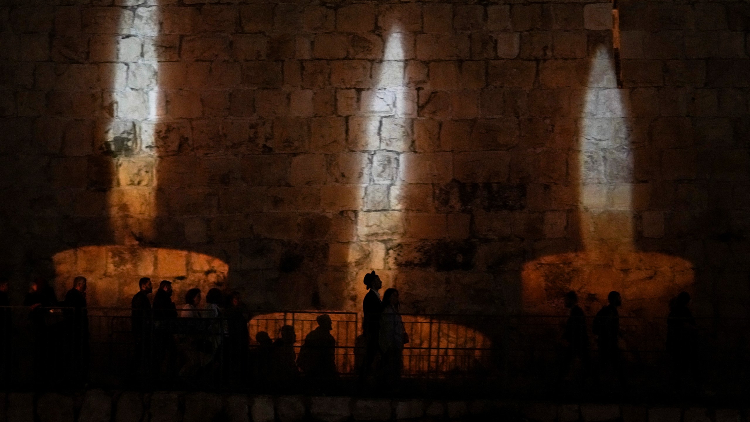 People walk by an image of memorial candles, projected on the walls of Jerusalem's Old City on the eve of annual Holocaust Remembrance Day, Monday, April 17, 2023. Israel holds the day of remembrance each year to remember the six million Jewish victims of the Nazi genocide during World War II. (AP Photo/Mahmoud Illean)