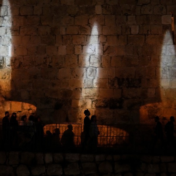 People walk by an image of memorial candles, projected on the walls of Jerusalem's Old City on the eve of annual Holocaust Remembrance Day, Monday, April 17, 2023. Israel holds the day of remembrance each year to remember the six million Jewish victims of the Nazi genocide during World War II. (AP Photo/Mahmoud Illean)