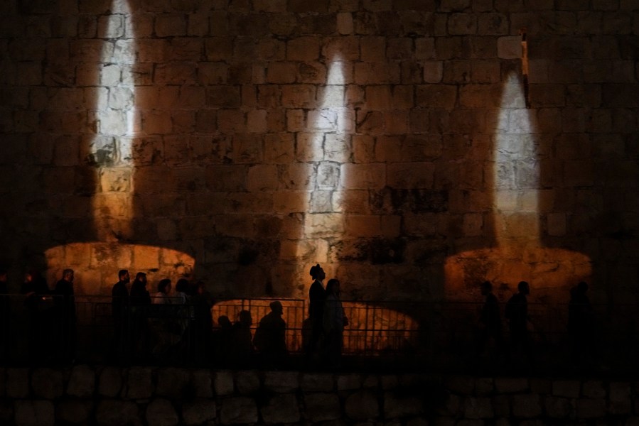 People walk by an image of memorial candles, projected on the walls of Jerusalem's Old City on the eve of annual Holocaust Remembrance Day, Monday, April 17, 2023. Israel holds the day of remembrance each year to remember the six million Jewish victims of the Nazi genocide during World War II. (AP Photo/Mahmoud Illean)