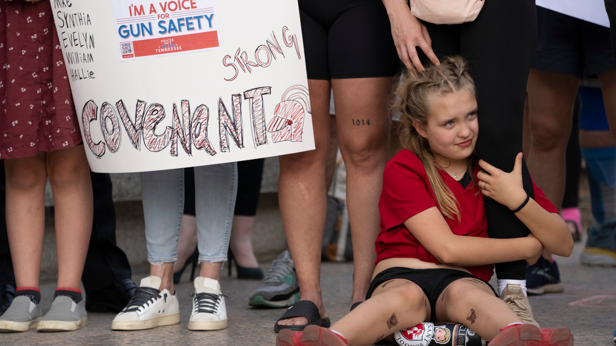 Covenant School student Alex Eissinger-Hansen holds her mother's leg during a demonstration for gun control legislation Tuesday, April 18, 2023, in Nashville, Tenn. Participants created a human chain spreading from Monroe Carell Jr. Children's Hospital at Vanderbilt, where victims of The Covenant School shooting were taken on March 27, to the Tennessee State Capitol. (AP Photo/George Walker IV)