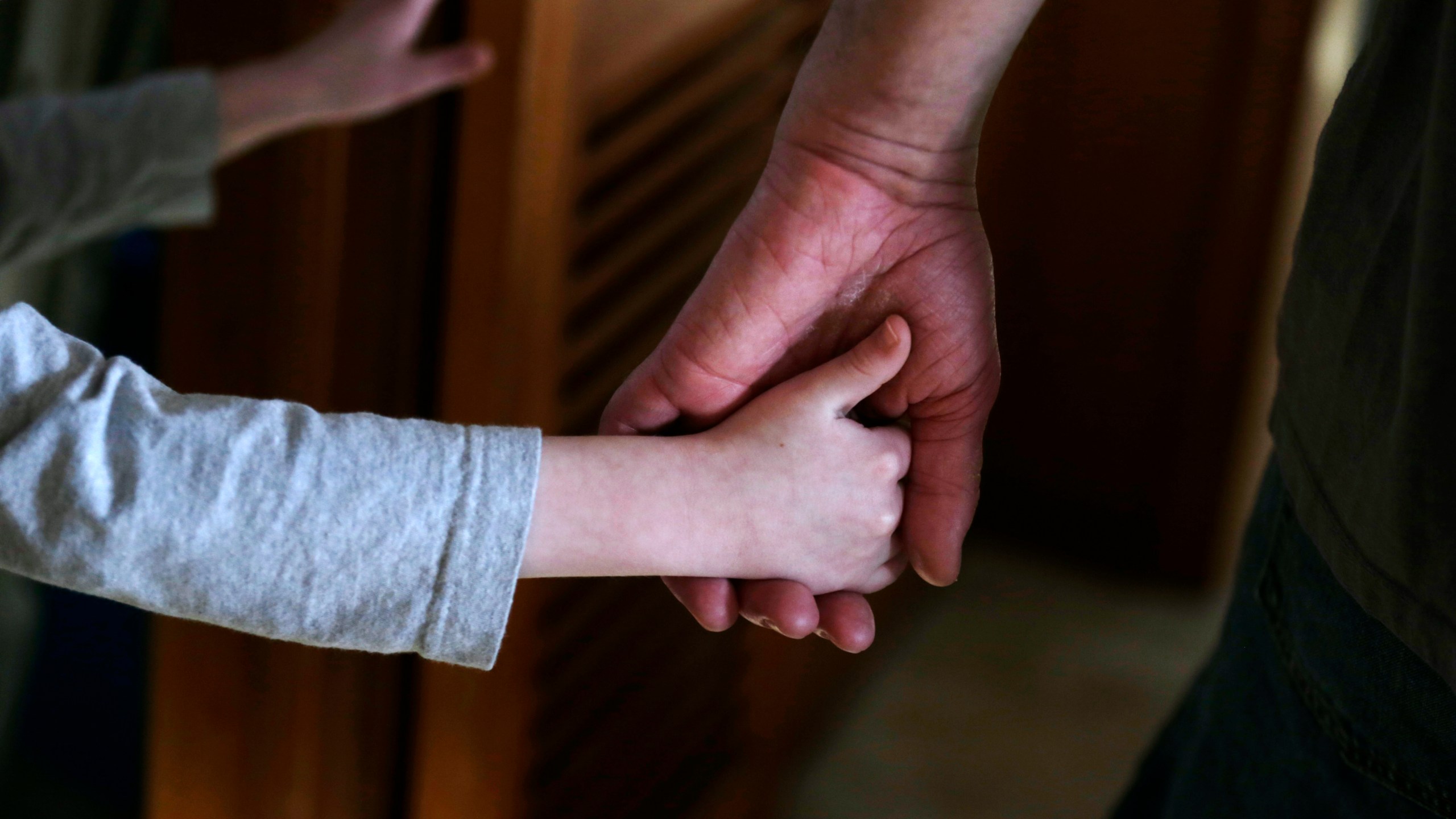 FILE - An autistic boy holds the hand of his adoptive father as they prepare to leave for a family outing from their home in Springfield, Mass., on Saturday, Dec. 12, 2015. Traditionally, autism was diagnosed only in kids with severe language and social impairments and unusual repetitious behaviors. But the definition gradually expanded, and autism is now shorthand for a group of milder, related conditions, too. (AP Photo/Charles Krupa, File)