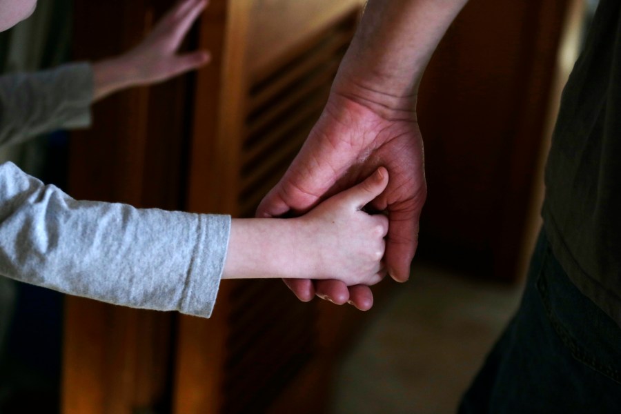 FILE - An autistic boy holds the hand of his adoptive father as they prepare to leave for a family outing from their home in Springfield, Mass., on Saturday, Dec. 12, 2015. Traditionally, autism was diagnosed only in kids with severe language and social impairments and unusual repetitious behaviors. But the definition gradually expanded, and autism is now shorthand for a group of milder, related conditions, too. (AP Photo/Charles Krupa, File)