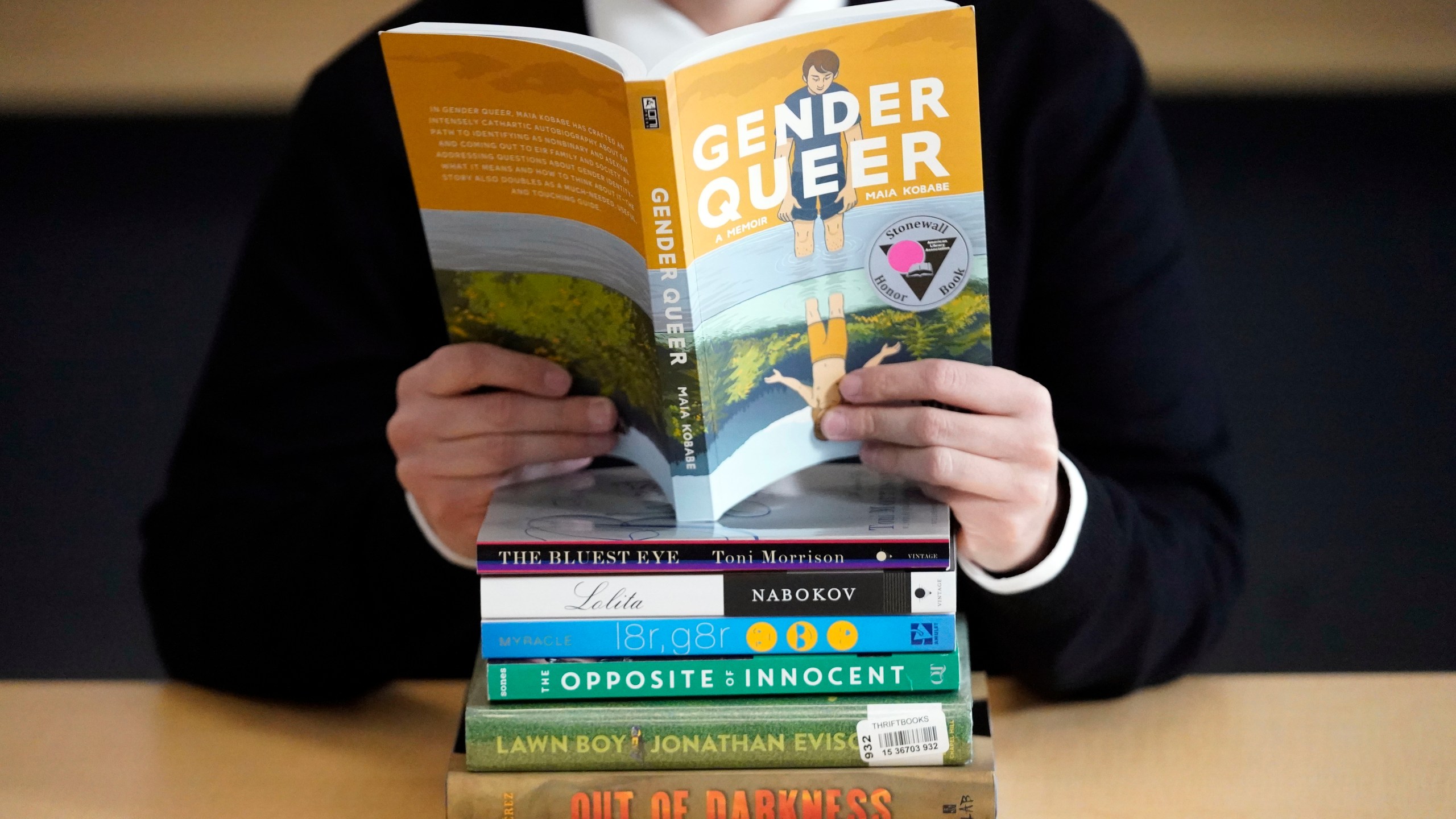 FILE - Amanda Darrow, director of youth, family and education programs at the Utah Pride Center, poses with books that have been the subject of complaints from parents on Dec. 16, 2021, in Salt Lake City. With legislators in Florida barring even the mention of being gay in classrooms and similar restrictions being considered in other states, books with LGBTQ+ themes remain the most likely targets of bans or attempted bans at public schools and libraries around the country, according to a new report Monday, April 24, 2023. Maia Kobabe’s graphic memoir “Gender Queer,” was the most “challenged” book of 2022, the second consecutive year it has topped the list. (AP Photo/Rick Bowmer, File)