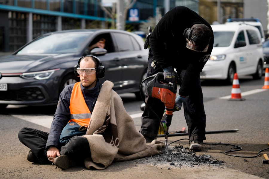 Police removes the pavement next to the hand of a climate activist during a protest against the climate policy of the German government in Berlin, Germany, Monday, April 24, 2023. German climate activists tried bringing traffic to a standstill in Berlin on Monday morning by gluing themselves to streets all over the capital. (AP Photo/Markus Schreiber)