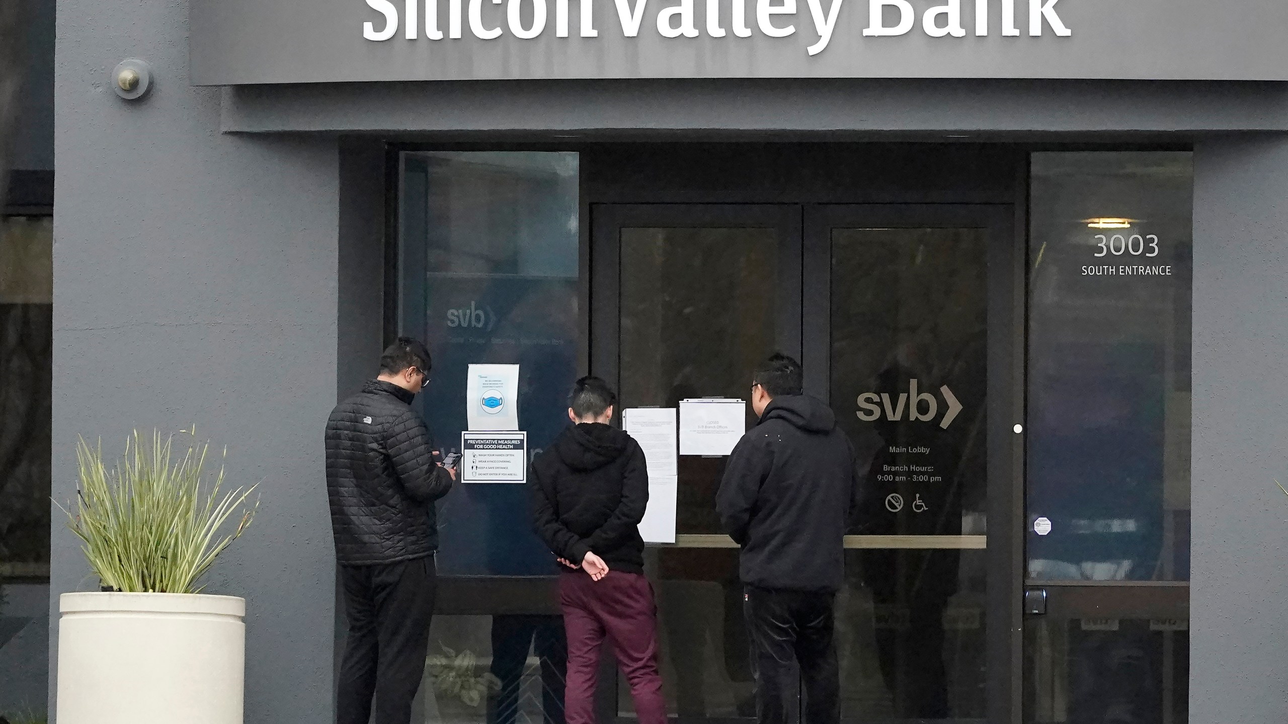 FILE - People look at signs posted outside of an entrance to Silicon Valley Bank in Santa Clara, Calif., Friday, March 10, 2023. In a sign fears about the global financial system have eased for now, major central banks are scaling back their offer of emergency dollar loans to banks, a crisis step launched after the collapse of Silicon Valley Bank in the U.S. fed fears about wider troubles. (AP Photo/Jeff Chiu, File)