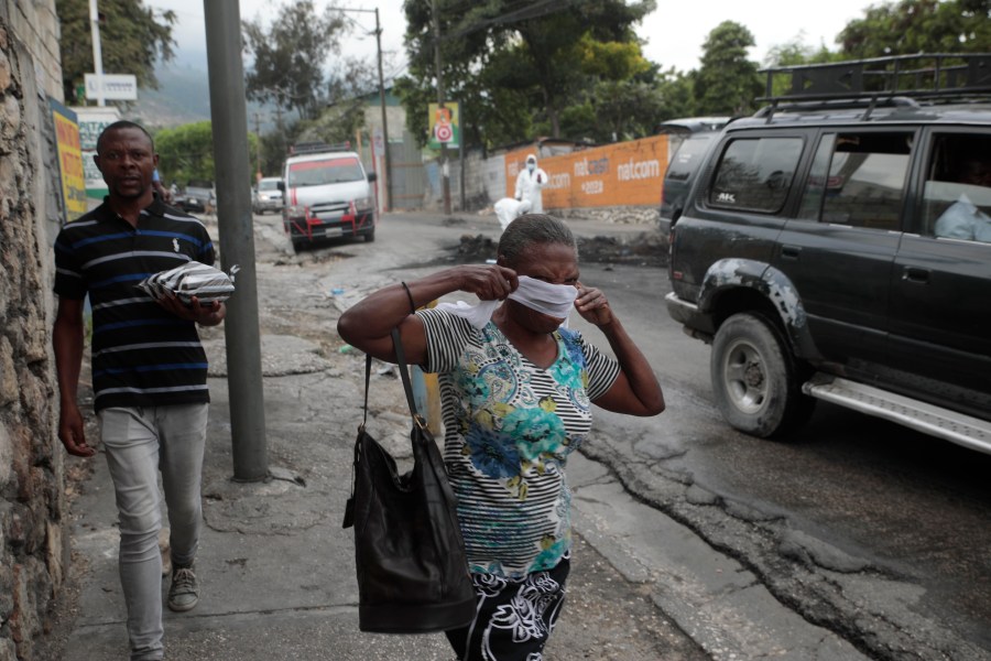 A woman walks past local authorities removing the bodies of men that were set on fire by a mob in Port-au-Prince, Haiti, Tuesday, April 25, 2023, a day after a mob pulled the 13 suspected gang members from police custody at a traffic stop and beat and burned them to death with gasoline-soaked tires. (AP Photo/Odelyn Joseph)