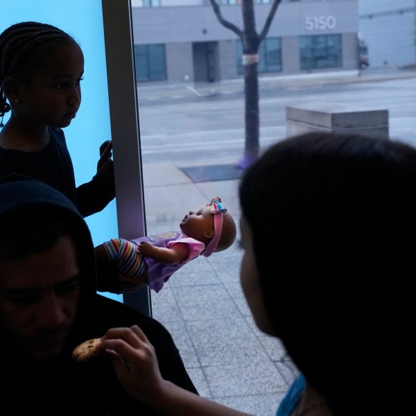 Charlotte, a Venezuelan immigrant, stands in silhouette holding a baby doll as her family and others take shelter in the Chicago Police Department's 16th District station on Monday, May 1, 2023. Chicago has seen the number of new arrivals grow tenfold in recent days. Shelter space is scarce and migrants awaiting a bed are sleeping on floors in police stations and airports. (AP Photo/Charles Rex Arbogast)