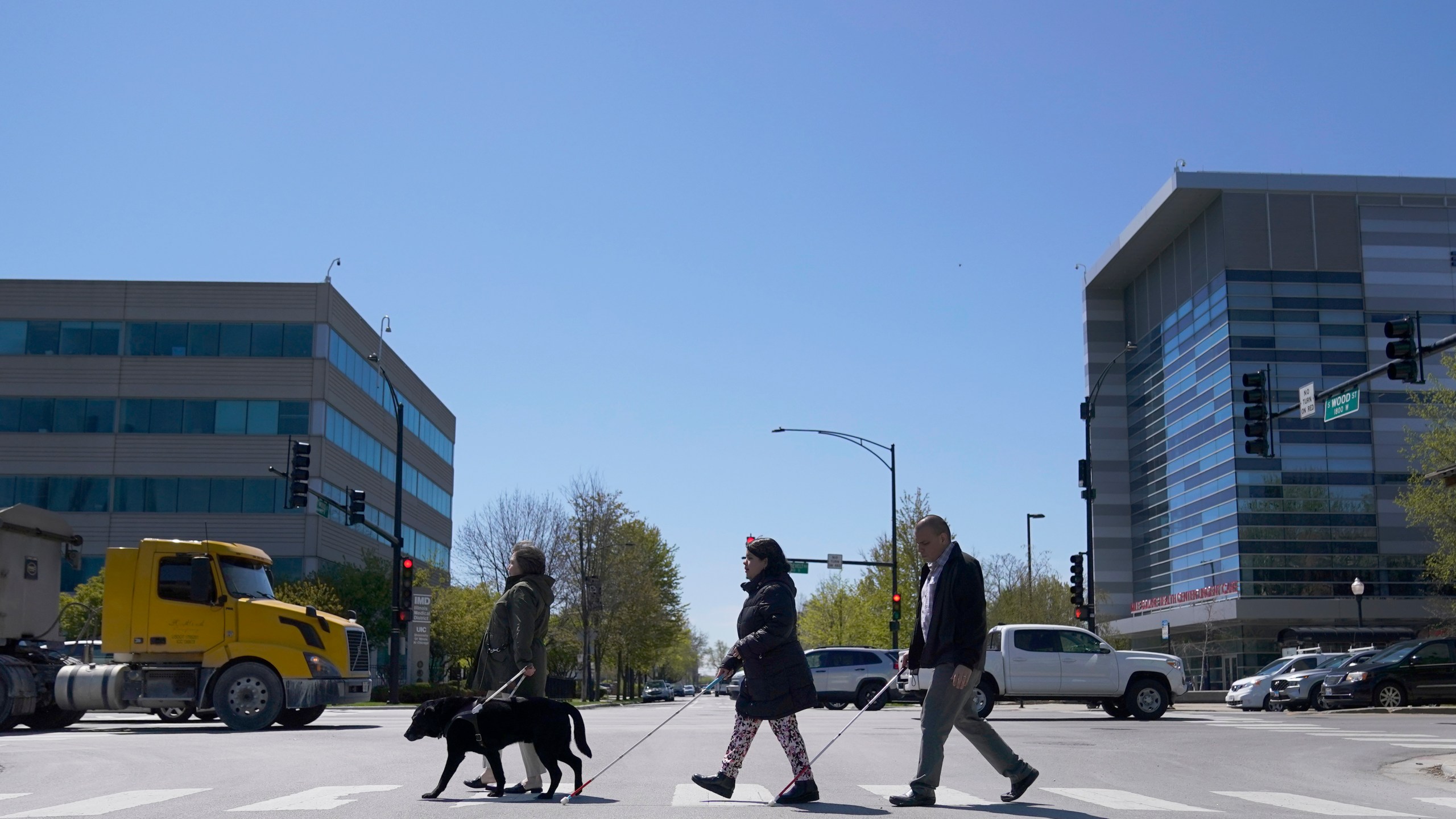 Maureen Reid, left, and her guide dog, Gaston, cross the intersection of Wood Street and Roosevelt Avenue with Sandy Murillo, center, and Geovanni Bahena, relying on an audible signal for the blind, on Wednesday, April 26, 2023, in Chicago. A federal court ruling slamming street crossing signals in Chicago as dangerous for blind and low-vision residents are giving momentum to advocates who say the community has long been left out of the push for safer streets. (AP Photo/Charles Rex Arbogast)