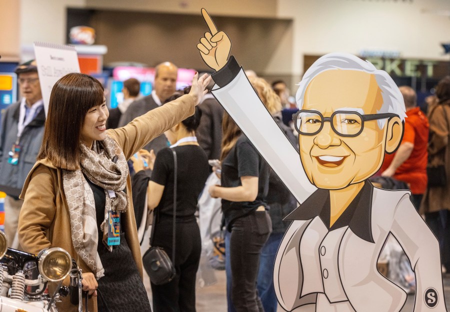 Hami Liu from Taiwan poses for a photo with a cardboard cutout of Warren Buffett at the See's Candies booth during the Berkshire Bazaar of Bargains at the CHI Health Center on Friday, May 5, 2023. (Chris Machian/Omaha World-Herald via AP)