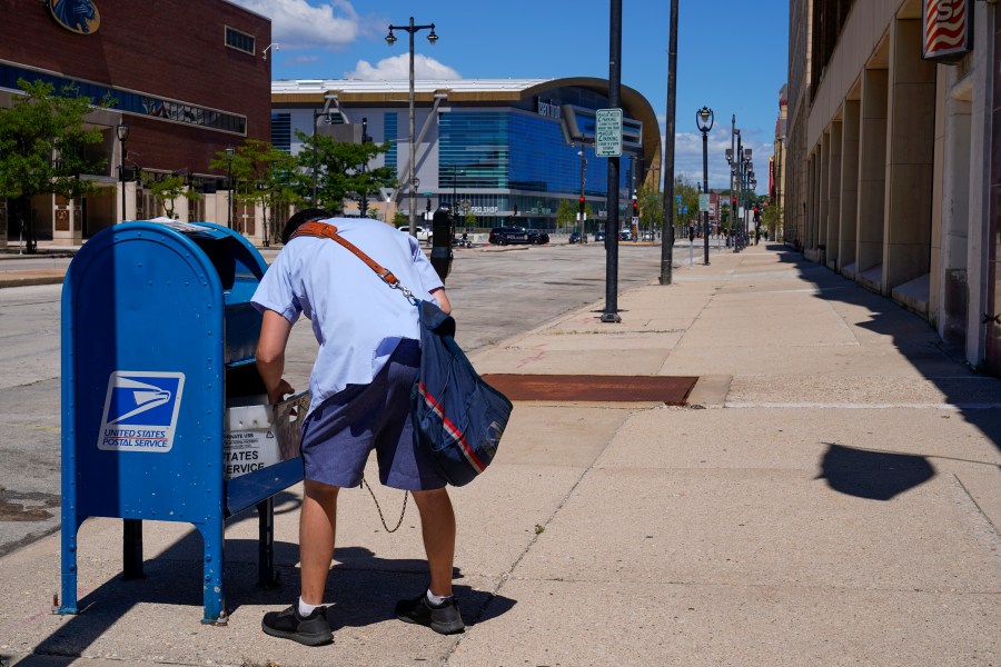 FILE - A postal worker empties a box near the Fiserv Forum on Aug. 18, 2020, in Milwaukee. Postal carriers have more worries than snow, rain or the gloom of night keeping them from their appointed rounds. These days, they're increasingly being robbed, often at gunpoint, from Maine to California. (AP Photo/Morry Gash, File)