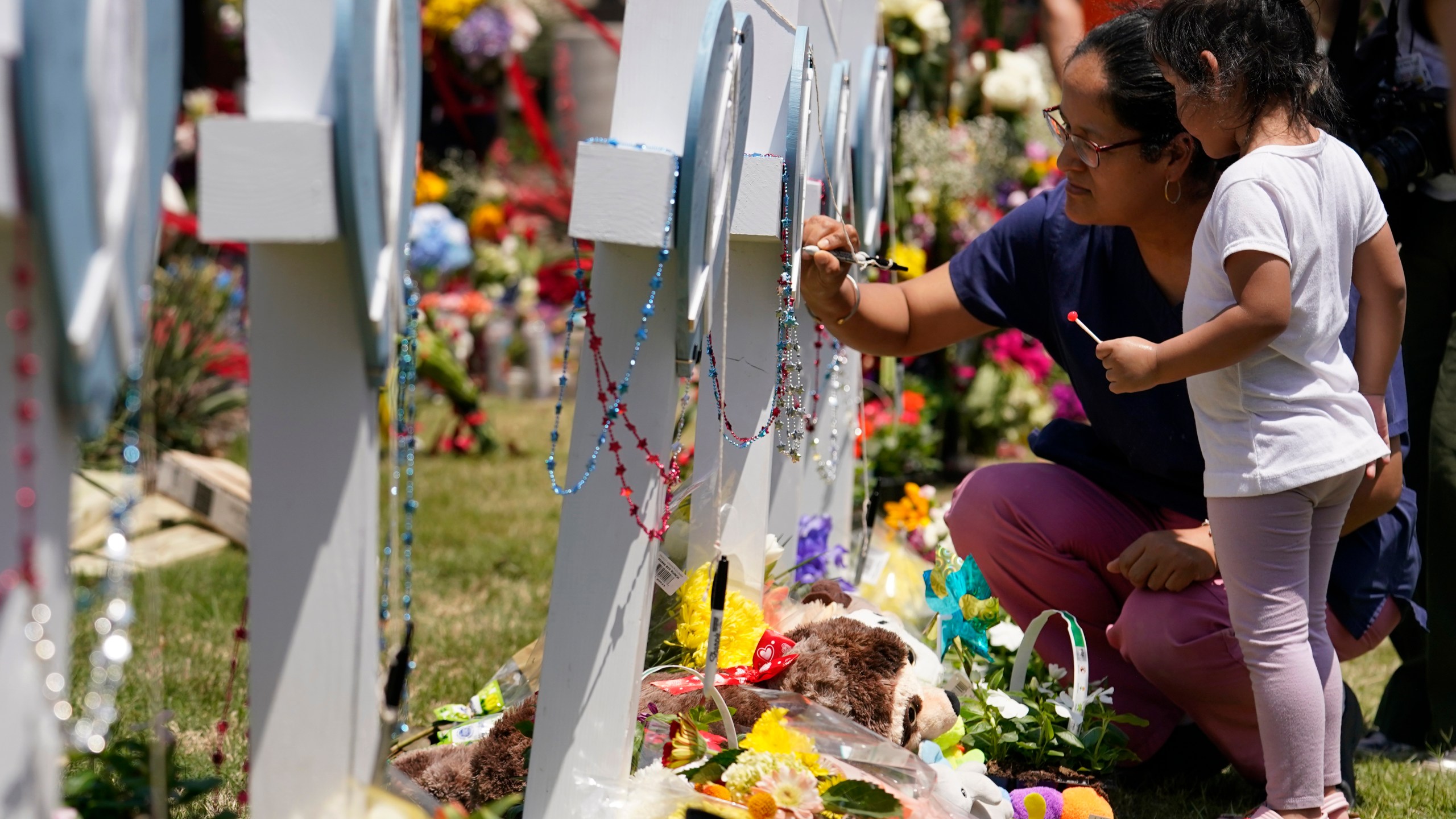 A woman signs a cross as a child looks on at a makeshift memorial by the mall where several people were killed in Saturday's mass shooting, Monday, May 8, 2023, in Allen, Texas. (AP Photo/Tony Gutierrez)