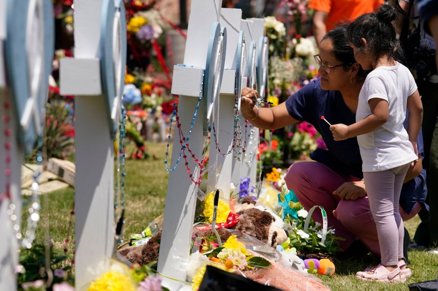 A woman signs a cross as a child looks on at a makeshift memorial by the mall where several people were killed in Saturday's mass shooting, Monday, May 8, 2023, in Allen, Texas. (AP Photo/Tony Gutierrez)