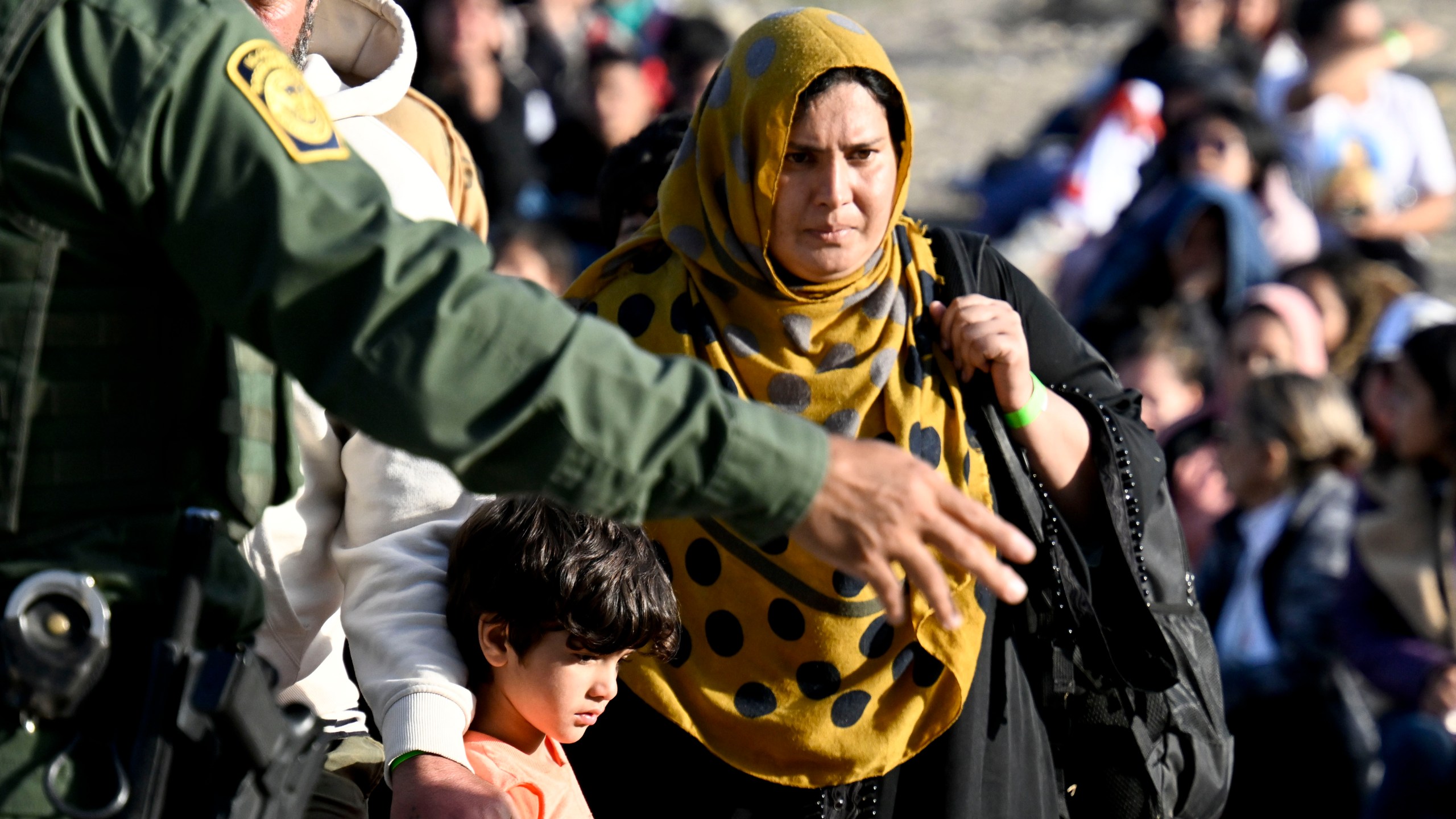 FILE - An asylum-seeker carries her baby past U.S. Border Patrol agents as they wait between the double fence along the U.S.-Mexico border near Tijuana, Mexico, Monday, May 8, 2023, in San Diego. As President Joe Biden's administration prepares for the end of asylum restrictions related to the COVID-19 pandemic, it is offering some new legal options for people — especially families — to come to the United States. The administration said it will admit at least 100,000 Latin Americans seeking to reunite with family members in the United States, but has released almost no details. (AP Photo/Denis Poroy, File)