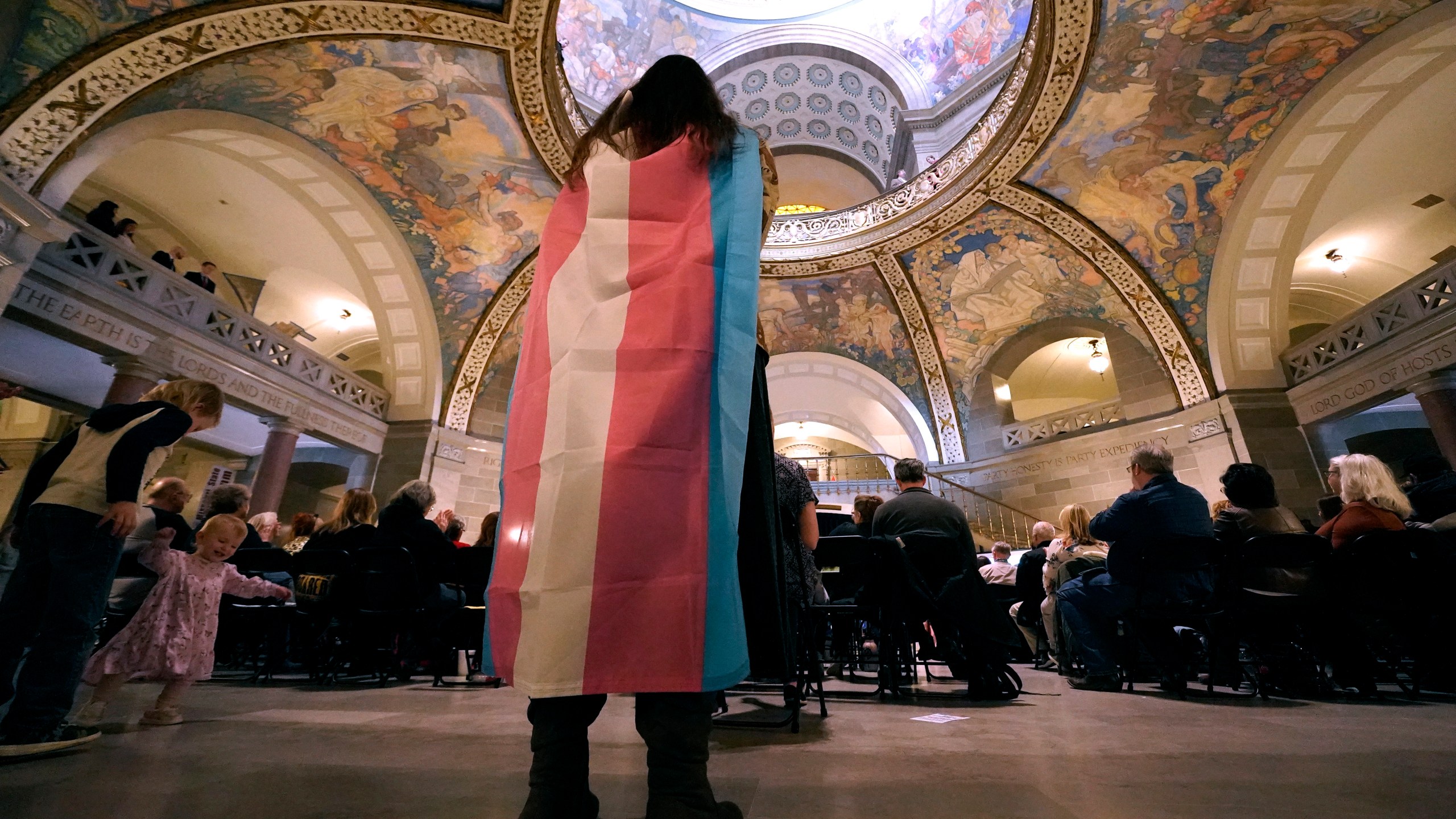 FILE - Glenda Starke wears a transgender flag as a counter protest during a rally in favor of a ban on gender-affirming health care legislation, March 20, 2023, at the Missouri Statehouse in Jefferson City, Mo. (AP Photo/Charlie Riedel, File)