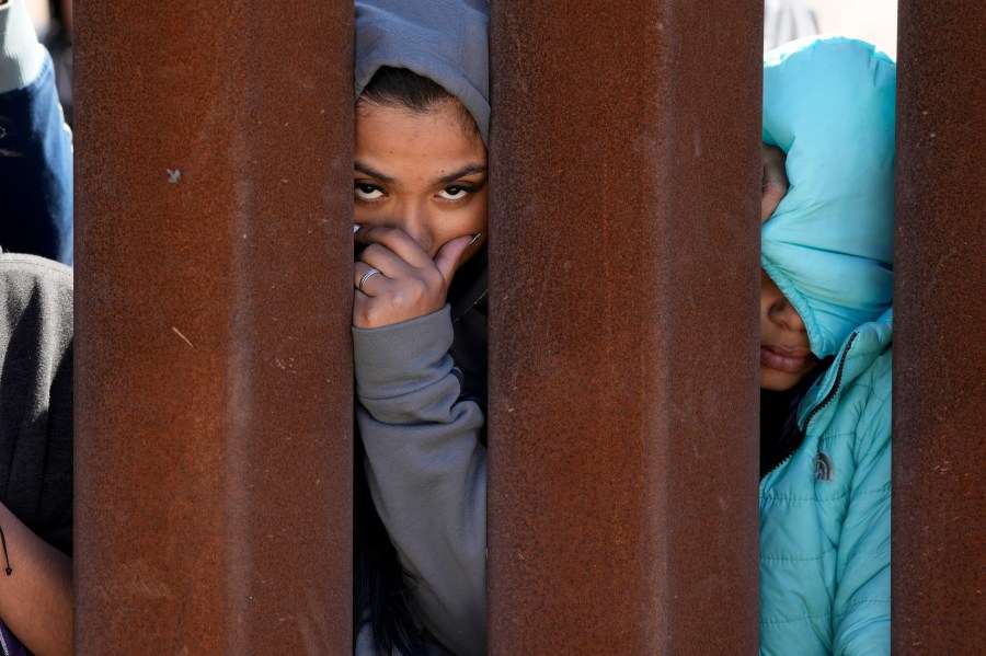 Migrants waiting to apply for asylum between two border walls look through the wall Thursday, May 11, 2023, in San Diego. Pandemic-related U.S. asylum restrictions, known as Title 42, are to expire May 11. (AP Photo/Gregory Bull)