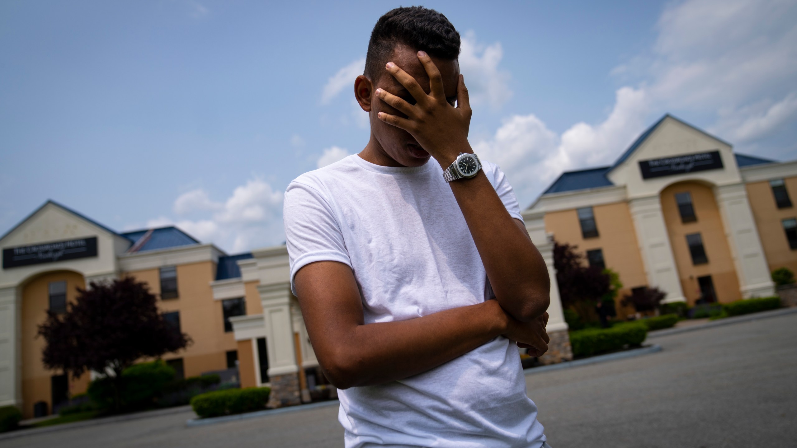 Mohamed, a 19-year-old fleeing political persecution in the northwest African country of Mauritania, poses for a photo that obscures his face to protect his identity, outside the Crossroads Hotel, before heading into town for a work opportunity, Monday, May 22, 2023, in Newburgh, N.Y. Mohamed is one of about 400 international migrants the city has been putting up in a small number of hotels in other parts of the state this month to relieve pressure on its overtaxed homeless shelter system. (AP Photo/John Minchillo)