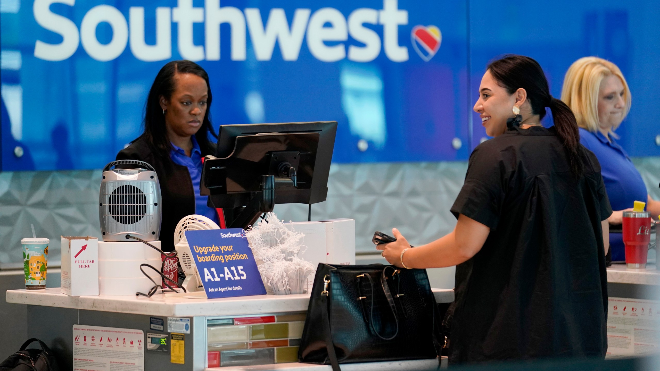 A Southwest airlines customer service representative, left, assists a traveler at the ticketing counter at Love Field airport, Friday, May 19, 2023, in Dallas. The unofficial start of the summer travel season is here, with airlines hoping to avoid the chaos of last year and travelers scrounging for ways to save a few bucks on pricey airfares and hotel rooms.(AP Photo/Tony Gutierrez)