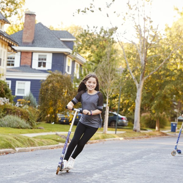 Three pre-teen girls playing in street on scooters and bike - stock photo