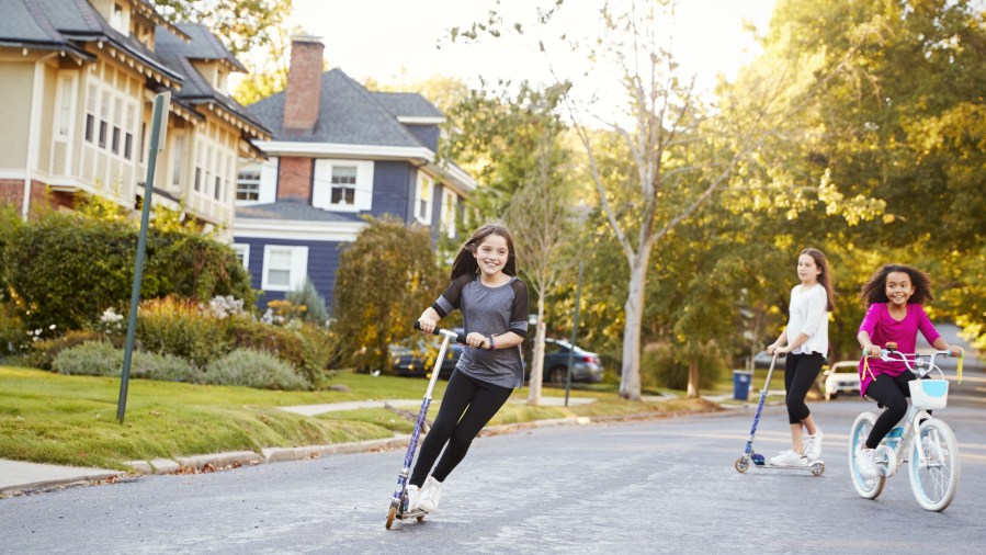 Three pre-teen girls playing in street on scooters and bike - stock photo