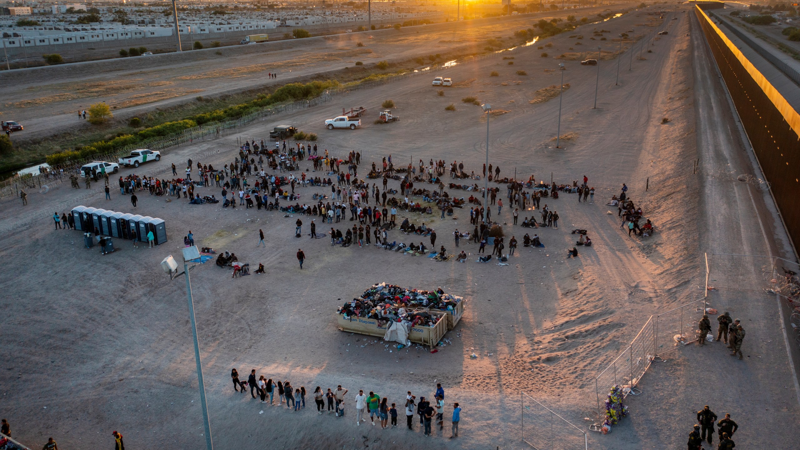 As the sun sets, migrants wait outside a gate in the border fence to enter into El Paso, Texas, to be processed by the Border Patrol, Thursday, May 11, 2023. (AP Photo/Andres Leighton)