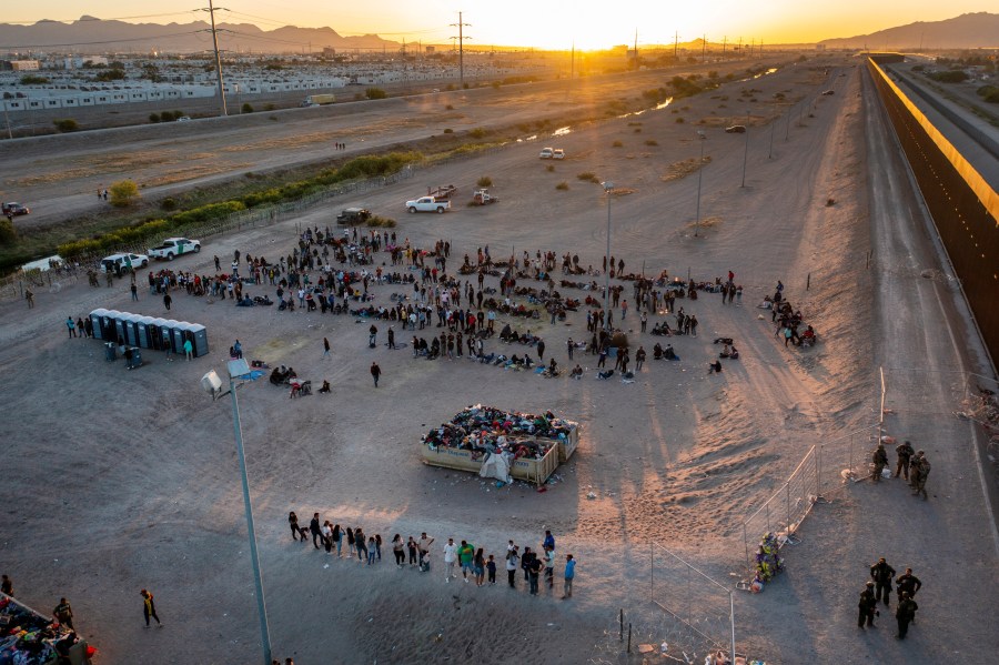 As the sun sets, migrants wait outside a gate in the border fence to enter into El Paso, Texas, to be processed by the Border Patrol, Thursday, May 11, 2023. (AP Photo/Andres Leighton)