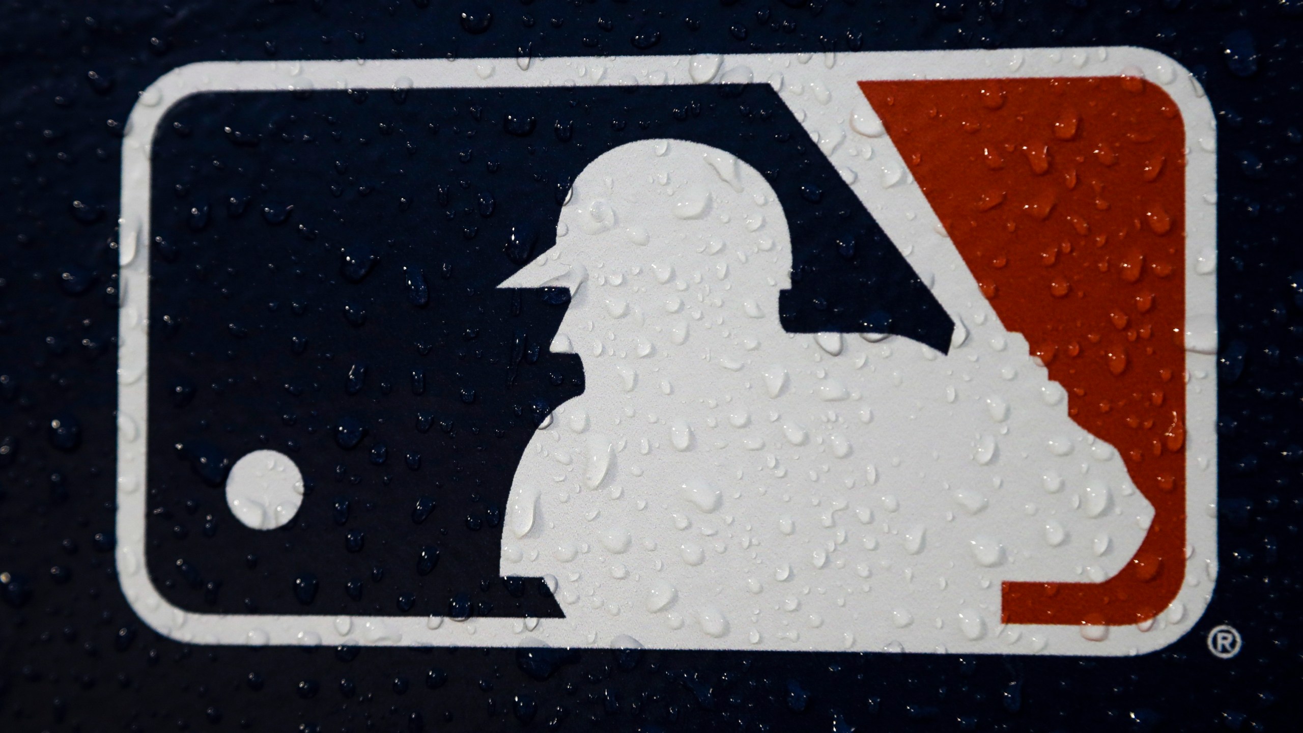 FILE - A rain-covered MLB logo is seen at Fenway Park before Game 1 of the World Series baseball game between the Boston Red Sox and the Los Angeles Dodgers, Oct. 23, 2018, in Boston. Seventeen former Major League Baseball scouts who say they were discriminated against because of their age sued the league, its teams and Commissioner Rob Manfred on Wednesday, June 21, 2023. (AP Photo/Matt Slocum, File)