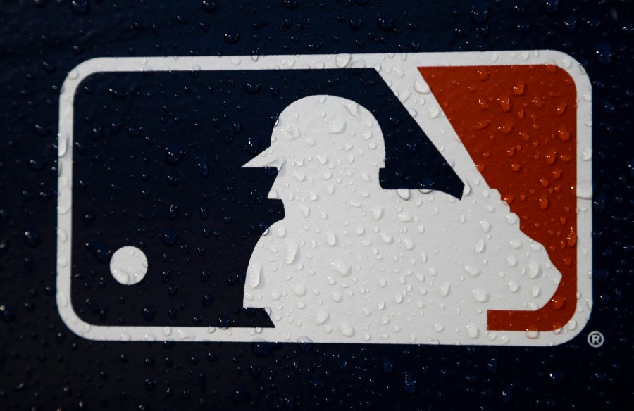 FILE - A rain-covered MLB logo is seen at Fenway Park before Game 1 of the World Series baseball game between the Boston Red Sox and the Los Angeles Dodgers, Oct. 23, 2018, in Boston. Seventeen former Major League Baseball scouts who say they were discriminated against because of their age sued the league, its teams and Commissioner Rob Manfred on Wednesday, June 21, 2023. (AP Photo/Matt Slocum, File)