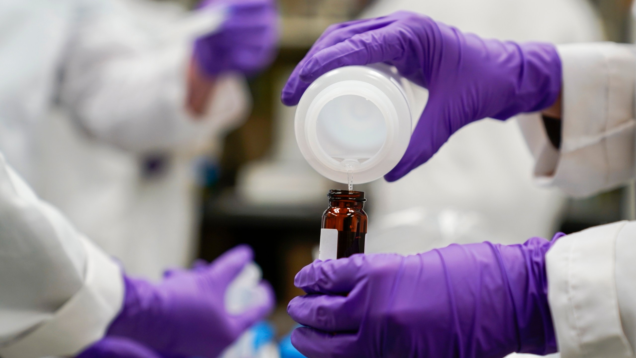 FILE - Eva Stebel, water researcher, pours a water sample into a smaller glass container for experimentation as part of drinking water and PFAS research at the U.S. Environmental Protection Agency Center For Environmental Solutions and Emergency Response on Feb. 16, 2023, in Cincinnati. The 3M chemical company announced Thursday, June, 22, 2023 a $10.3 billion settlement with U.S. water utilities and agencies over PFAS pollution that will allow them to test and treat drinking water contaminated with these “forever chemicals.(AP Photo/Joshua A. Bickel, File)