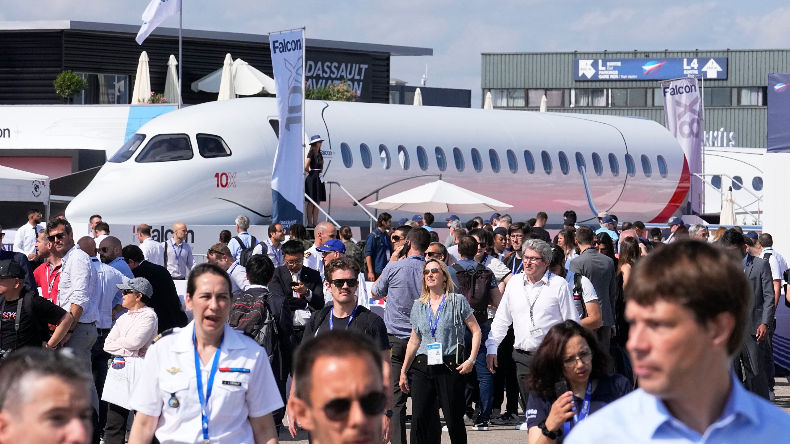 FILE - Visitors walk by a Falcon 10X prototype by the French manufacturer Dassault Aviation, at the Paris Air Show, Wednesday, June 21, 2023 in Le Bourget, north of Paris. Airlines are facing increasing pressure to cut their climate-changing emissions. That made sustainable aviation fuel a hot topic this week at the Paris Air Show, a major industry event. Sustainable fuel made from food waste or plant material is aviation's best hope for reducing emissions in the next couple of decades. (AP Photo/Michel Euler, File)