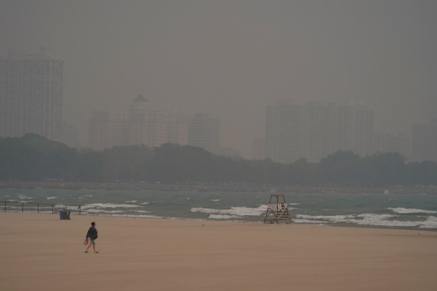 A person walks on Montrose Beach as buildings behind the shore are blanketed in haze from Canadian wildfires Tuesday, June 27, 2023, in Chicago. (AP Photo/Kiichiro Sato)