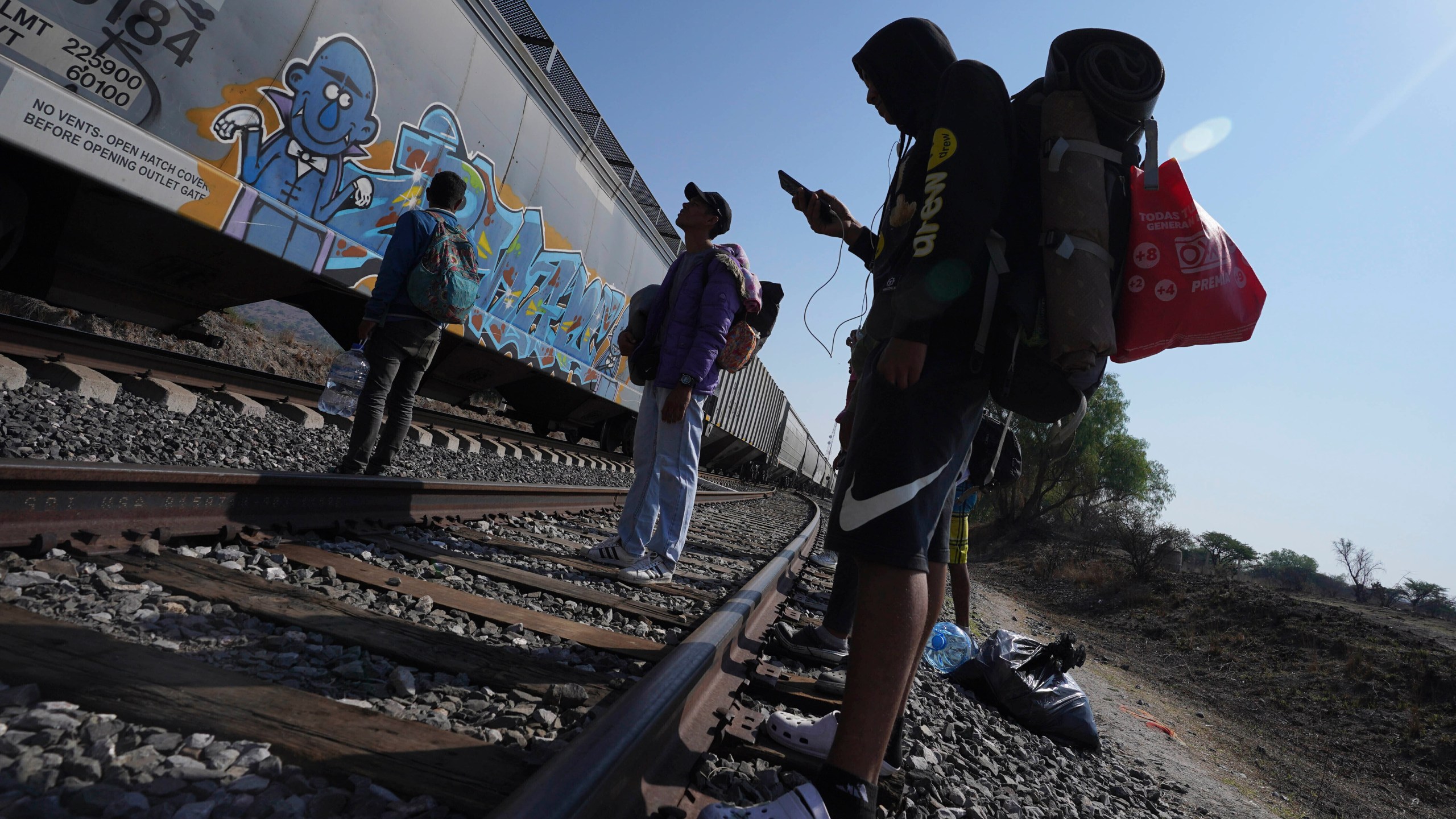 FILE - Migrants watch a train go past as they wait along the train tracks hoping to board a freight train heading north, one that stops long enough so they can hop on, in Huehuetoca, Mexico, May 12, 2023, the day after U.S. pandemic-related asylum restrictions called Title 42 were lifted. Unwittingly, migrants in Latin America finance disinformation during their journeys to the U.S., as they fall victim to fraud that can cost them thousands of dollars and that in turn has served to develop new business models, from fake work recruiters to those who call themselves "migration coaches." (AP Photo/Marco Ugarte, File)