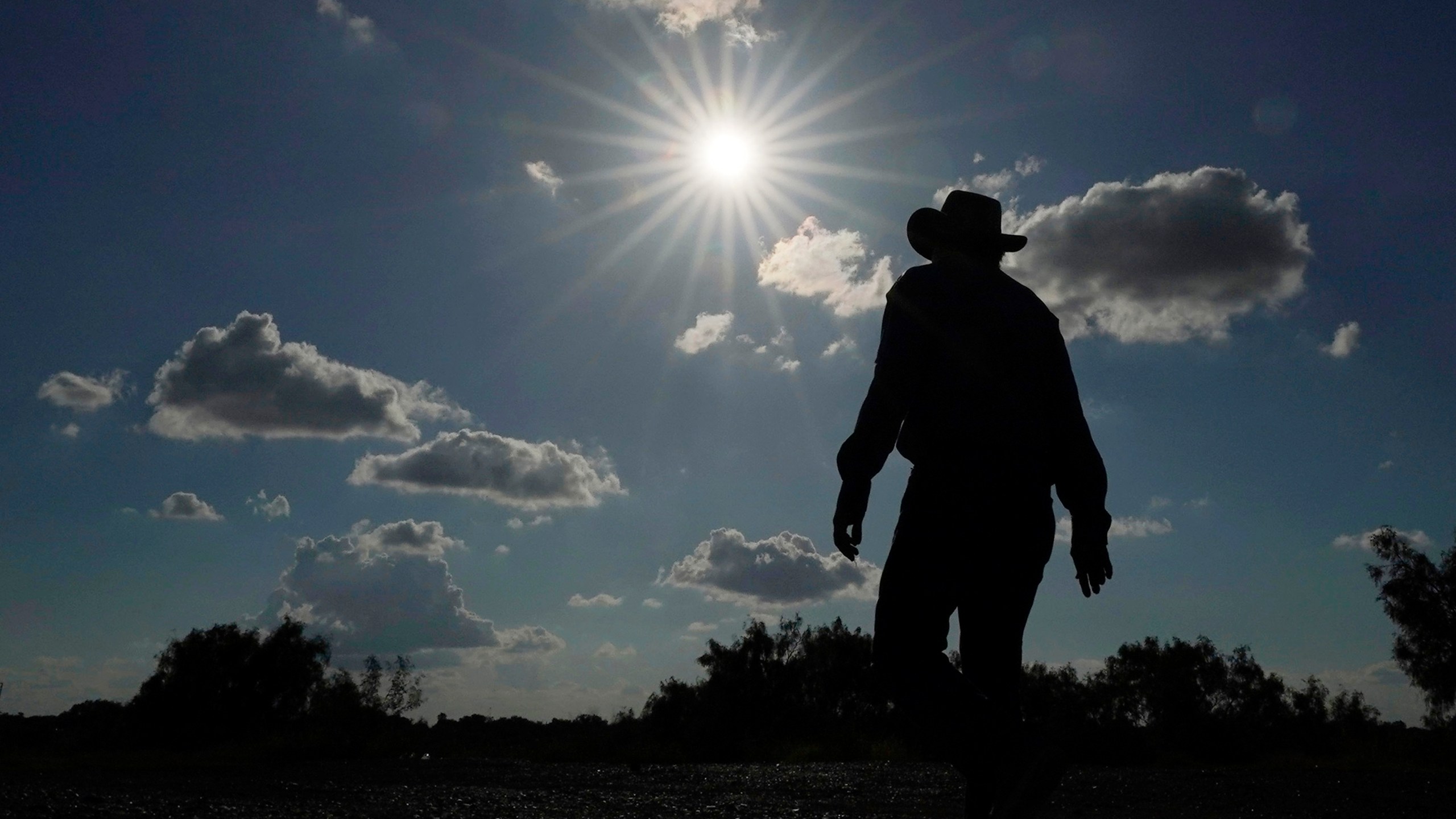 FILE - Kayak and canoe outfitter Jessie Fuentes walks along the Rio Grande under a warm sun Thursday, July 6, 2023. As the heat breaks records, weakening and sickening people, it’s worth remembering that dire heat waves have inspired effective efforts to prevent heat illness. (AP Photo/Eric Gay, File)