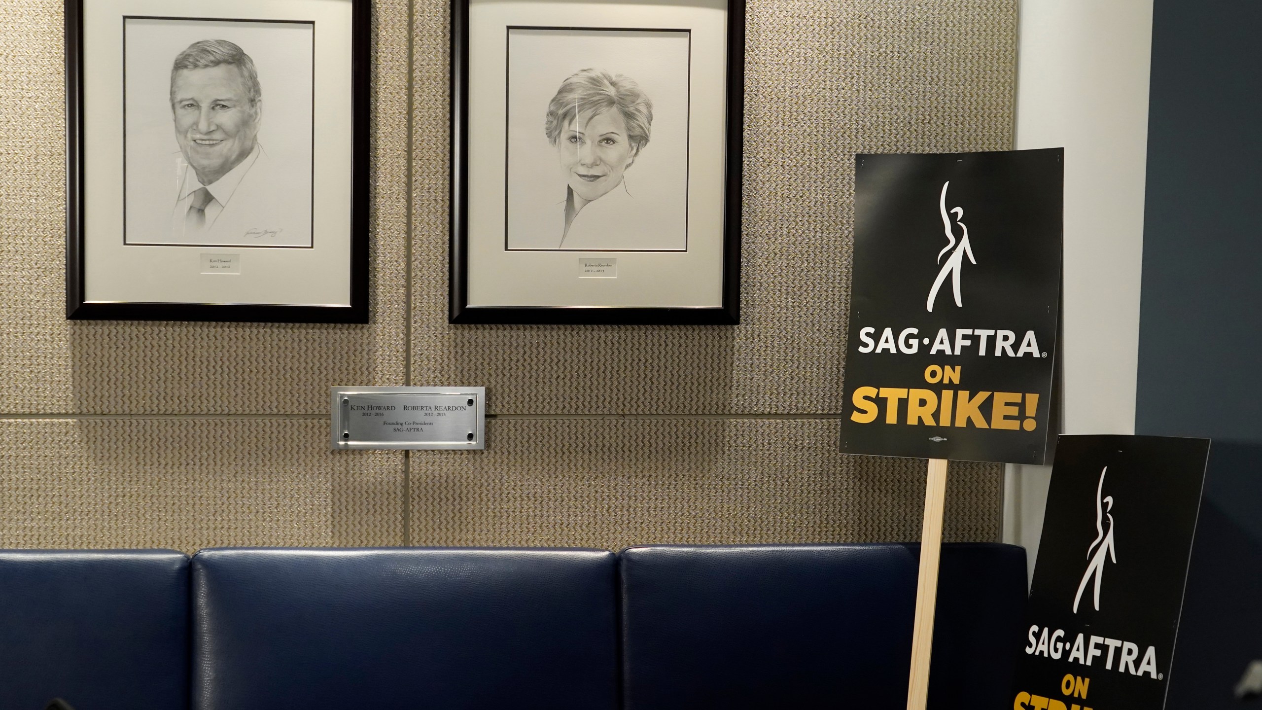 Portraits of SAG-AFTRA founding co-presidents Ken Howard and Roberta Reardon hang next to strike signage following a press conference announcing a strike by The Screen Actors Guild-American Federation of Television and Radio Artists on Thursday, July, 13, 2023, in Los Angeles. This marks the first time since 1960 that actors and writers will picket film and television productions at the same time. (AP Photo/Chris Pizzello)